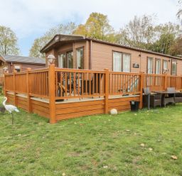 A wooden mobile home with a fenced deck and outdoor chairs on grass at 27 Lake View in Cawston