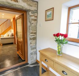 A hallway with a wooden console table and a vase with red roses near a window and a view into a room with a staircase and a sofa at Yr Hen Stabal in Trawsfynydd