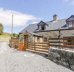 A stone house with dormer windows and wooden fences on a gravel driveway at Yr Hen Stabal in Trawsfynydd