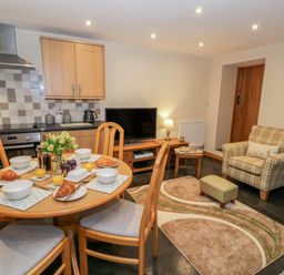 A kitchen and living area with a round dining table set with croissants orange juice and flowers at Yr Hen Stabal in Trawsfynydd