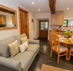 A living area with a gray sofa with cushions and a wooden dining table set with breakfast at Yr Hen Stabal in Trawsfynydd