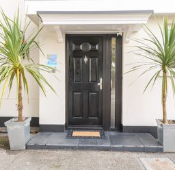 A black front door with a doormat and two potted plants on either side at Babbacombe Hall in Babbacombe