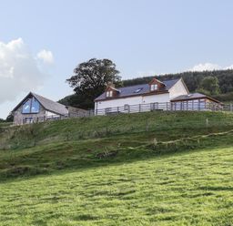 A farmhouse and barn on a grassy hillside with trees and a forest in the background at Tyn Llwyn Barn in Glyndyfrdwy near Llangollen