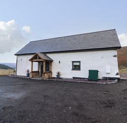 A single-story white building with a slate roof and a wooden porch in a rural landscape at Tyn Llwyn Barn in Glyndyfrdwy near Llangollen