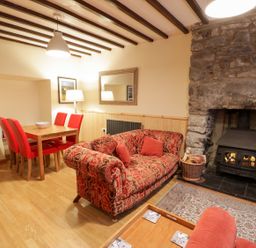 A living room with a patterned red sofa a dining table with red chairs and a stone fireplace at Edrydd in Harlech