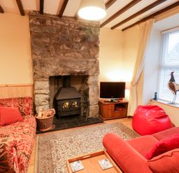 A living room with red sofas red bean bag a stone fireplace and a television at Edrydd in Harlech