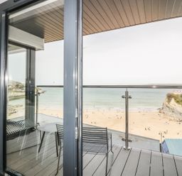 A balcony with a table and chairs overlooking a beach and ocean at Onshore 7 in Newquay