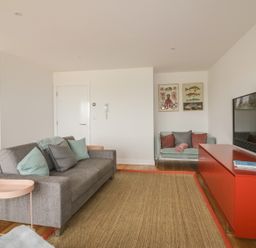 A living room with a grey sofa and a small turquoise couch a red cabinet with a tv and a lamp Onshore 7 Newquay
