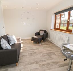 A sitting area with a sofa armchair and ottoman near a window and a wall clock at Afon Rhos Bach in Llanrug