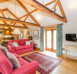 A living room with red sofas wooden beams a patterned rug and a small wall-mounted television at Middle Farm Annex in Long Bredy