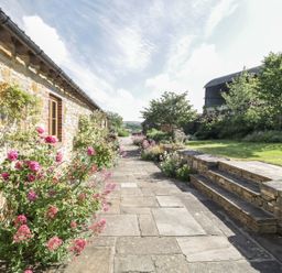 A stone building with windows and flowers along a paved pathway next to stone steps and greenery at Middle Farm Annex in Long Bredy