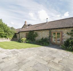 An exterior view of a stone building with a tiled roof a grass lawn and paved patio with shrubs and plants at Middle Farm Annex in Long Bredy