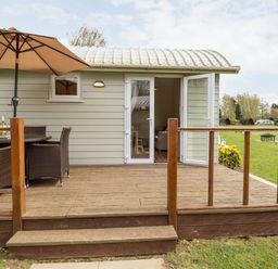 A wooden deck with a table umbrella and chairs outside a small building with glass doors at Bramble in Banham
