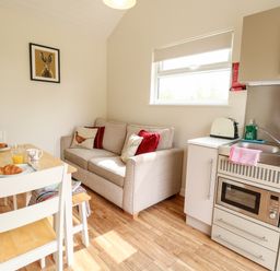 A kitchen and dining area with a sofa a wooden dining table with chairs and a small kitchen unit with a microwave and sink at Bramble in Banham