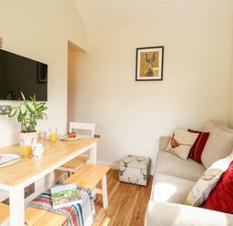 A small dining area with a wooden table set with plates and orange juice beside a beige sofa in a living room at Bramble in Banham