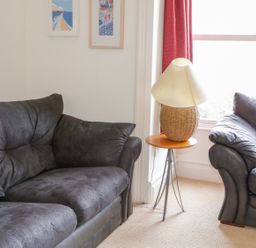 A living room with two dark sofas a small side table with a lamp and framed pictures on the wall at 1 Orchard Cottages Salcombe