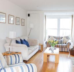 A living room with striped armchairs and sofas a wooden coffee table with flowers and a television at 1 Orchard Cottages in Salcombe