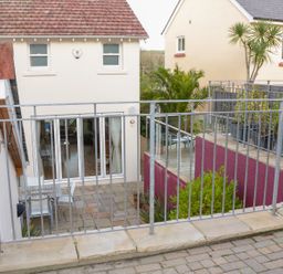 An outdoor patio area with a metal railing and a table with chairs near cream colored buildings at 1 Orchard Cottages in Salcombe