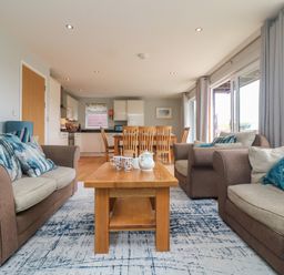 A living room with brown and beige sofas around a wooden coffee table and a dining table with chairs in the background at Lodge Sixty Six in St Columb Major