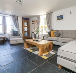 A living room with a sofa armchair wooden coffee table and a window at Miner's Rest in Troon near Camborne