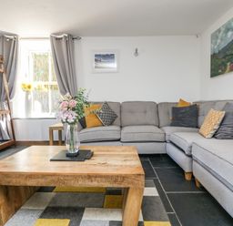 A living room with a gray sectional sofa and wooden coffee table with flowers at Miner's Rest in Troon near Camborne