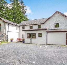 Exterior view of a white stone house with multiple windows and a gravel driveway at Stiniog Lodge in Blaenau Ffestiniog
