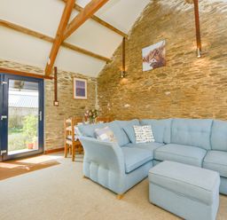 A living room with a blue sectional sofa a matching ottoman a wooden dining table with chairs and glass doors at Erin Cottage in Pelynt near Looe