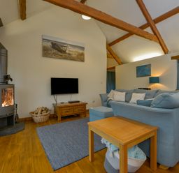 A living room with a wood stove a blue sofa a wooden table and a television at Hook Cottage in Pelynt near Looe