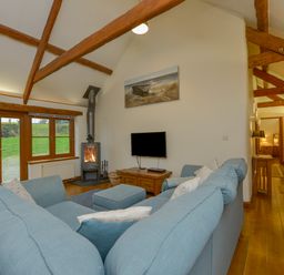 A living room with blue sofas a wood stove and wooden beams on the ceiling at Hook Cottage in Pelynt near Looe