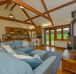 An open plan living room and kitchen with blue sofas a wood stove and wooden beams at Hook Cottage in Pelynt near Looe
