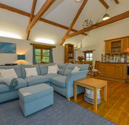 An open living room and kitchen with a blue sectional sofa wooden beams and a dining table at Hook Cottage in Pelynt near Looe