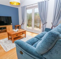 A living room with a blue sofa wooden coffee table and television at 1 Lake View in Lanreath