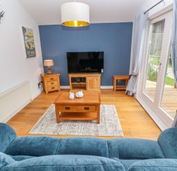 A living room with a blue sofa wooden furniture and glass doors at 1 Lake View in Lanreath