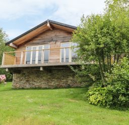 A wooden house with a stone base surrounded by greenery and trees at 1 Lake View in Lanreath
