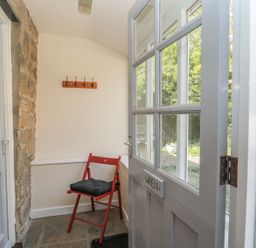 A small entryway with a red chair with a cushion stone wall and a white door at Wren Cottage in Morpeth