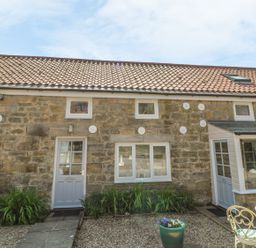 Stone cottage exterior with two doors two windows plants in front and outdoor table and chairs at Heron Cottage in Morpeth