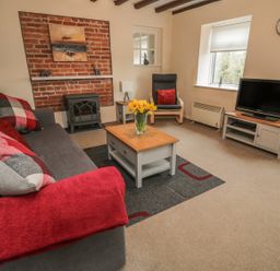 A living room with a sofa and cushions a coffee table and tv at Magpie Cottage in Morpeth