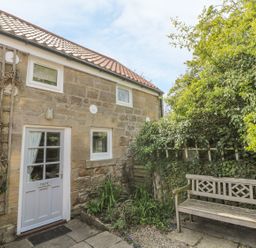 Stone cottage exterior with white door and windows garden bench and greenery at Magpie Cottage in Morpeth