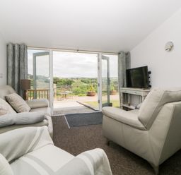 A living room with leather sofas a television and open glass doors leading to a patio with outdoor furniture at Owl Barn in Tavistock
