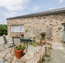 An outdoor patio area with a stone wall house a glass table with chairs and potted plants at Owl Barn in Tavistock