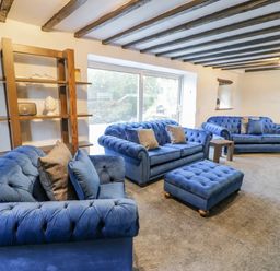 A living room with blue sofas a matching ottoman wooden shelves and exposed ceiling beams at Cae Lleci Llanfachreth near Dolgellau