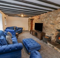 A living room with blue sofas a wooden tv stand and a wood burning stove at Cae Lleci in Llanfachreth near Dolgellau