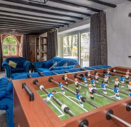 A game room with a foosball table and blue upholstered sofas with exposed ceiling beams and stone walls at Cae Lleci Llanfachreth near Dolgellau