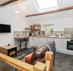 A kitchen with white cabinets wooden countertop bar stools and a brown leather sofa at La'al Riddings in Lowick Green Riddings Farm Near Ulverston