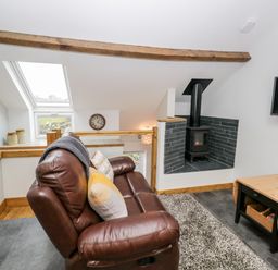 A living space with a brown leather sofa pillows a wood stove a wall clock a small wooden table and a skylight window at La'al Riddings in Lowick Green Riddings Farm Near Ulverston