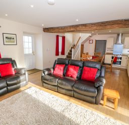 A living room with black leather sofas and red cushions next to an open kitchen with wooden dining table at Stabl in Pwllheli
