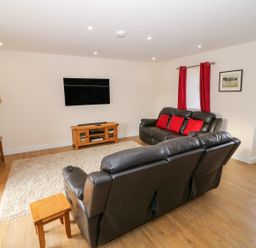 A living room with two black sofas red cushions red curtains a wooden tv stand and a wall mounted tv at Stabl in Pwllheli