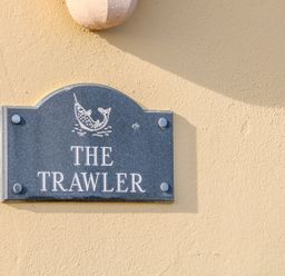 A dark sign with a fish illustration and the text The Trawler on a beige wall at The Trawler in Blackwater County Wexford