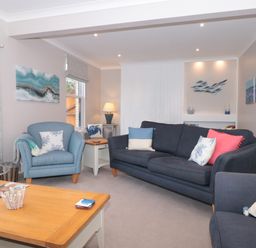 A living room with blue and grey sofas and armchairs a wooden coffee table and coastal artwork at Moorings in Kingswear Devon
