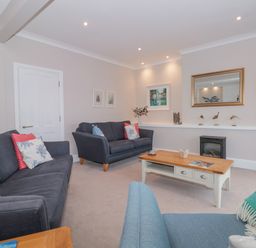 A living room with two dark grey sofas a light blue armchair a wooden coffee table and a wall-mounted television at Moorings in Kingswear Devon